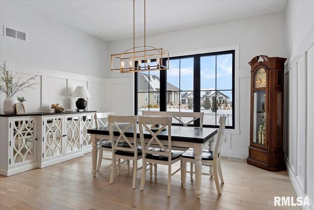 dining area featuring an inviting chandelier, a decorative wall, a wainscoted wall, light wood-type flooring, and visible vents