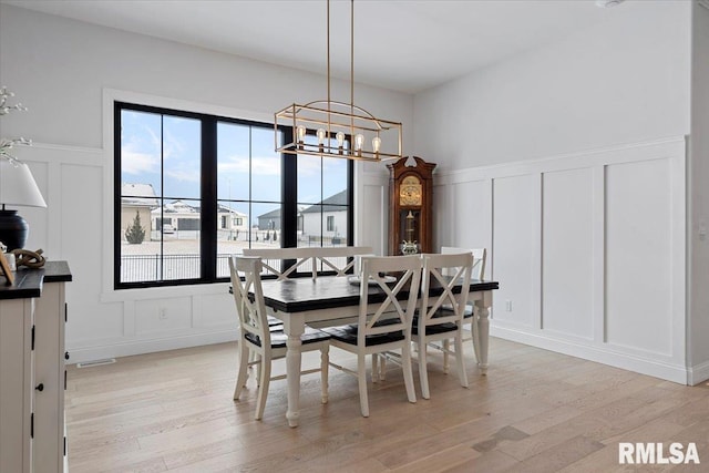 dining room featuring wainscoting, a decorative wall, light wood-style flooring, and a chandelier