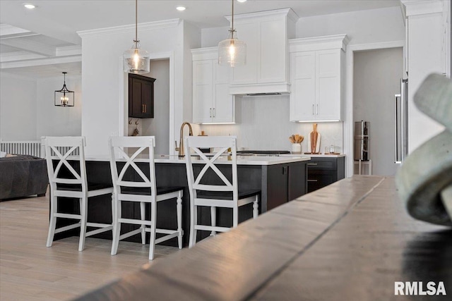 kitchen with light countertops, light wood finished floors, a kitchen bar, and white cabinetry