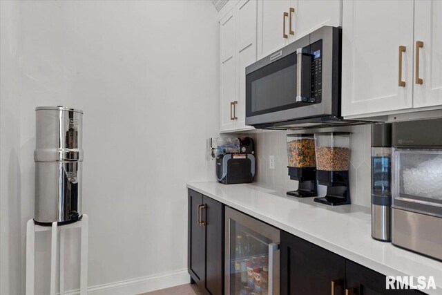 kitchen with white cabinets, stainless steel microwave, baseboards, decorative backsplash, and wine cooler