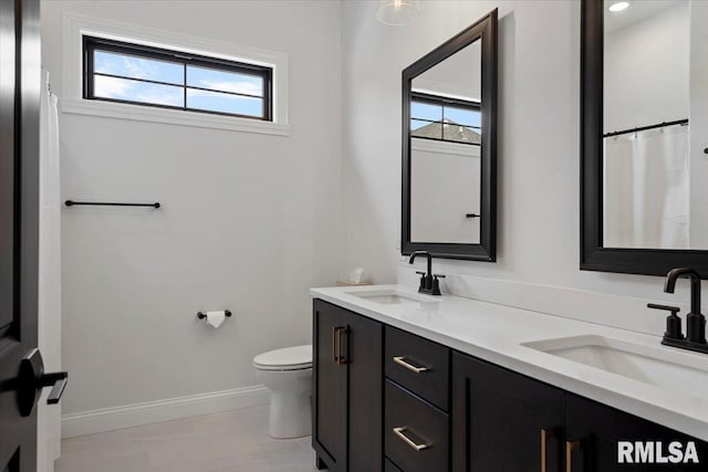 bathroom with baseboards, a sink, double vanity, and toilet