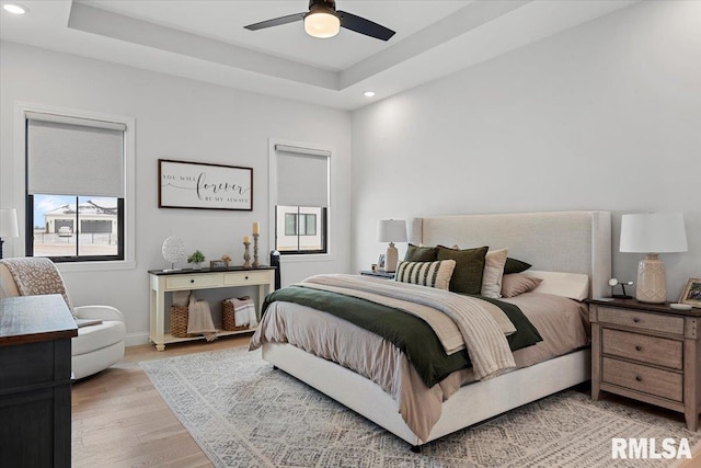 bedroom featuring light wood finished floors, recessed lighting, baseboards, a ceiling fan, and a tray ceiling