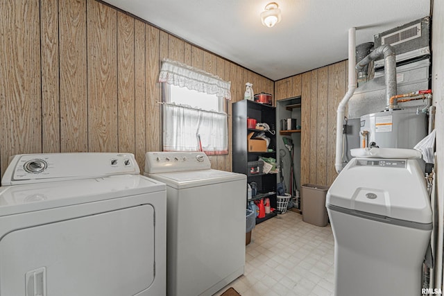 washroom featuring washer and dryer, electric water heater, and wood walls