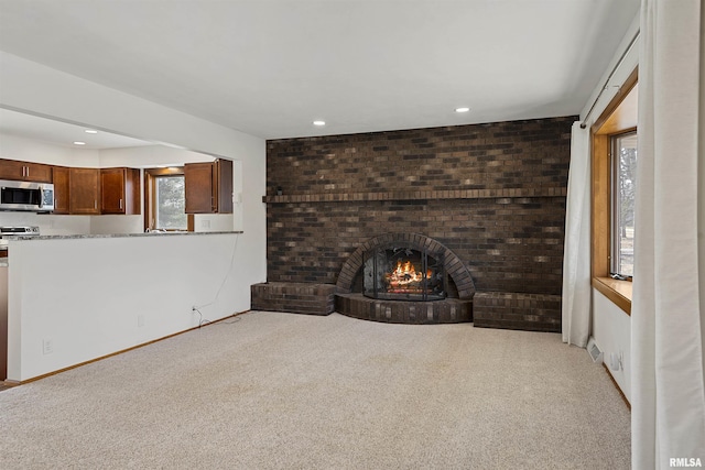 unfurnished living room with a wealth of natural light, a brick fireplace, light colored carpet, and recessed lighting