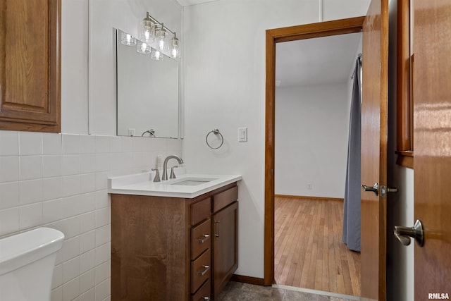 bathroom with toilet, wood finished floors, vanity, and tile walls