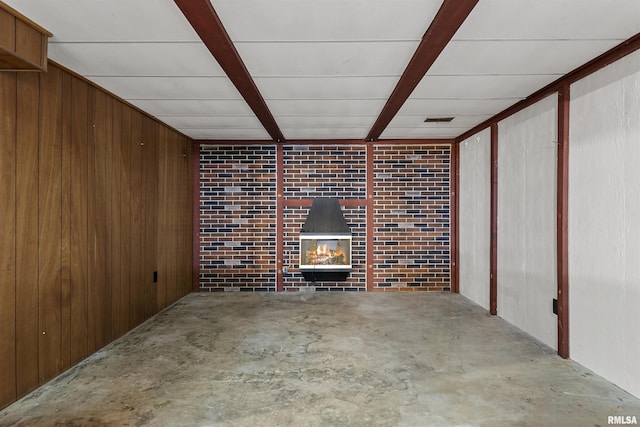 interior space with wooden walls, beamed ceiling, concrete flooring, and a tile fireplace