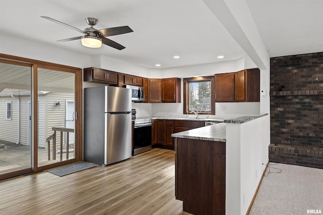 kitchen featuring brick wall, a peninsula, a sink, appliances with stainless steel finishes, and light wood-type flooring