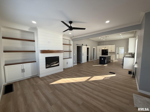 unfurnished living room featuring ornamental molding, a ceiling fan, a barn door, and baseboards