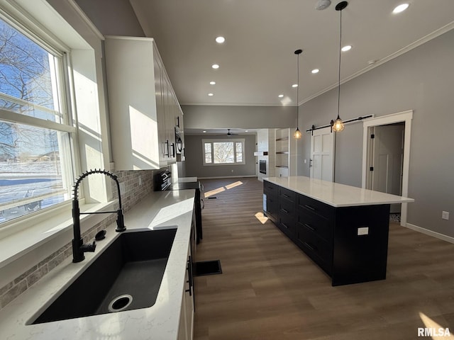 kitchen with dark cabinets, ornamental molding, a sink, baseboards, and open floor plan