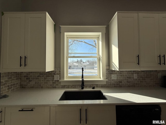 kitchen with tasteful backsplash, dishwasher, white cabinets, and a sink