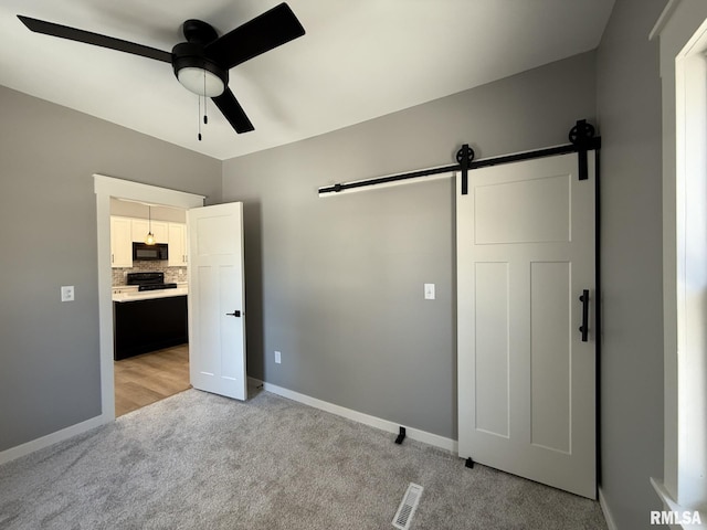 unfurnished bedroom featuring a barn door, a ceiling fan, visible vents, baseboards, and light colored carpet