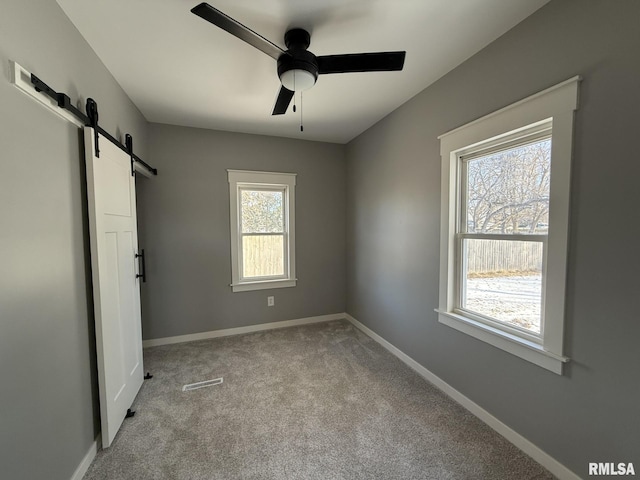 unfurnished bedroom with carpet flooring, multiple windows, a barn door, and baseboards