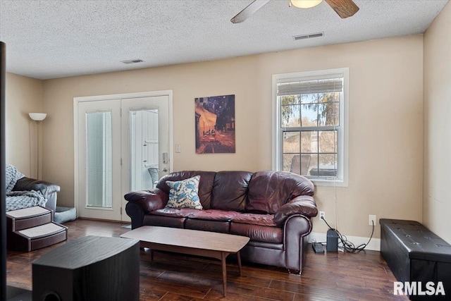 living area featuring dark wood-type flooring, visible vents, a textured ceiling, and a ceiling fan