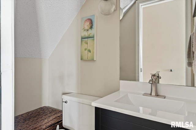 bathroom with lofted ceiling, a textured ceiling, toilet, and vanity