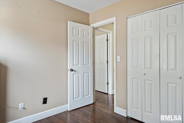 unfurnished bedroom featuring a textured ceiling, baseboards, dark wood-type flooring, and a closet