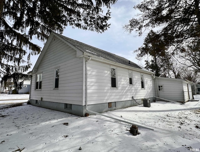 snow covered property with central air condition unit and roof with shingles