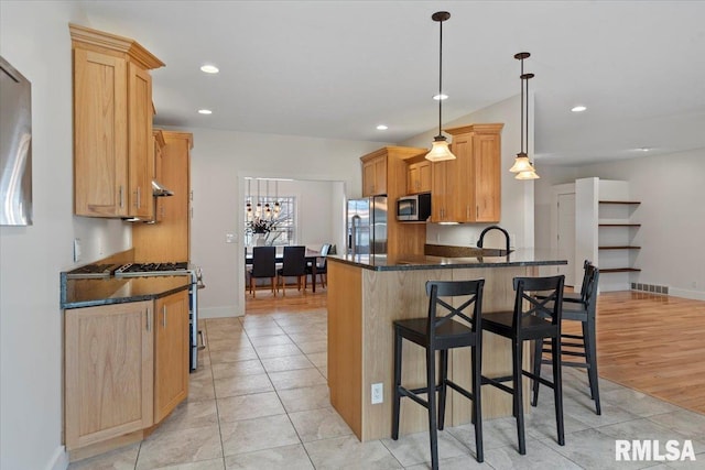 kitchen with pendant lighting, visible vents, appliances with stainless steel finishes, a sink, and dark stone countertops