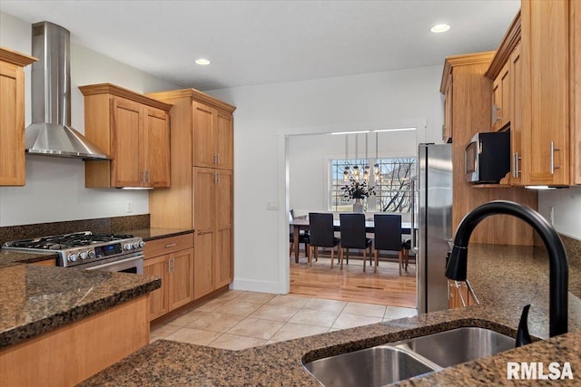 kitchen featuring light tile patterned floors, stainless steel appliances, hanging light fixtures, dark stone counters, and wall chimney exhaust hood