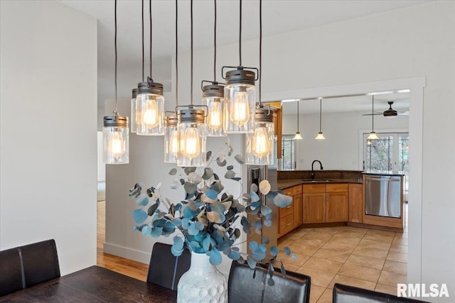 kitchen featuring pendant lighting, dark countertops, brown cabinetry, a sink, and dishwasher