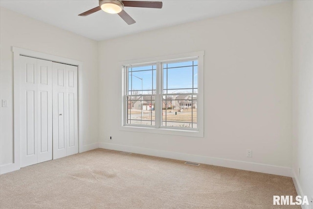 unfurnished bedroom featuring a closet, visible vents, light carpet, ceiling fan, and baseboards