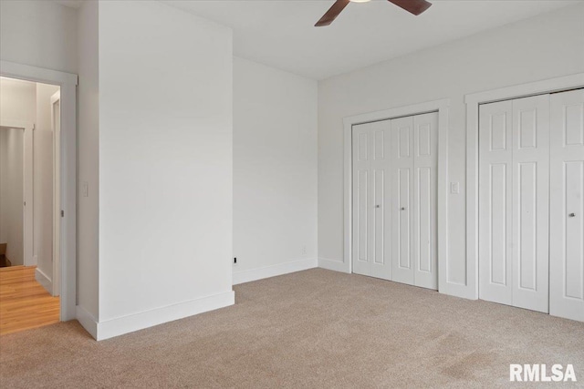 unfurnished bedroom with light carpet, two closets, a ceiling fan, and baseboards