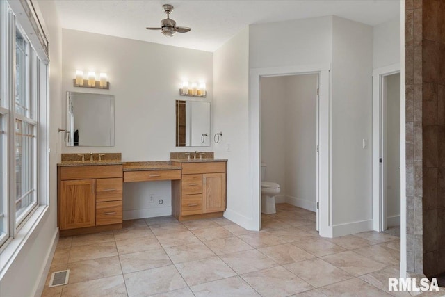 full bathroom with double vanity, visible vents, toilet, a ceiling fan, and plenty of natural light