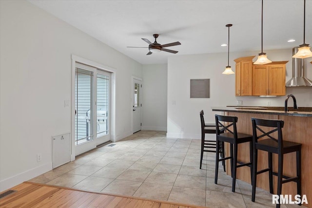 kitchen featuring a kitchen bar, dark countertops, visible vents, hanging light fixtures, and wall chimney exhaust hood