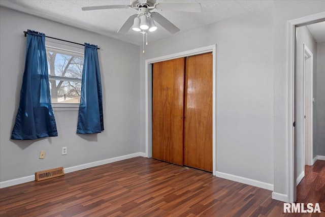 unfurnished bedroom featuring a textured ceiling, dark wood-style flooring, visible vents, and baseboards