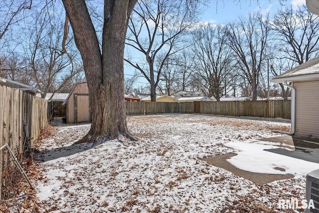 yard layered in snow with a storage shed, a fenced backyard, and an outbuilding