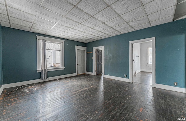 empty room featuring plenty of natural light, dark wood-style floors, an ornate ceiling, and baseboards