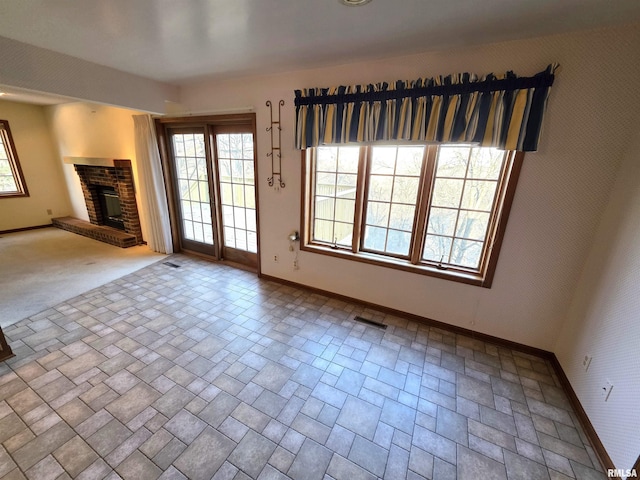 unfurnished living room with a brick fireplace, visible vents, and baseboards