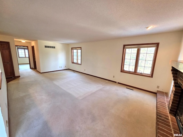 unfurnished living room with light carpet, a brick fireplace, visible vents, and a wealth of natural light