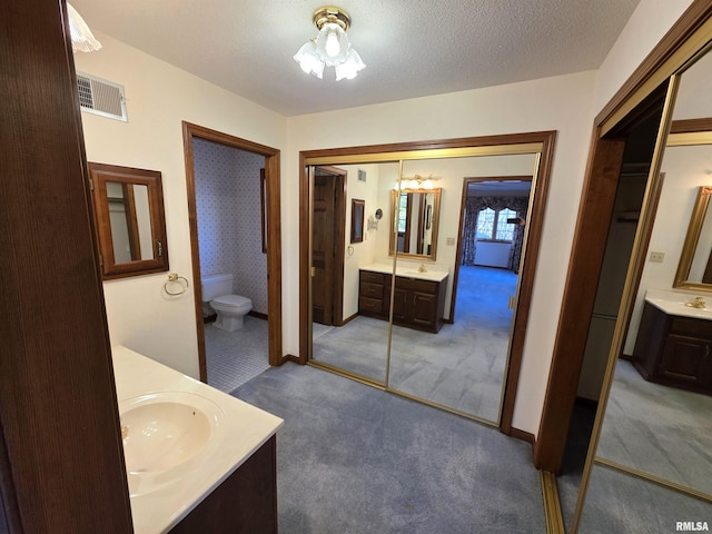 full bathroom featuring a textured ceiling, toilet, two vanities, a sink, and visible vents