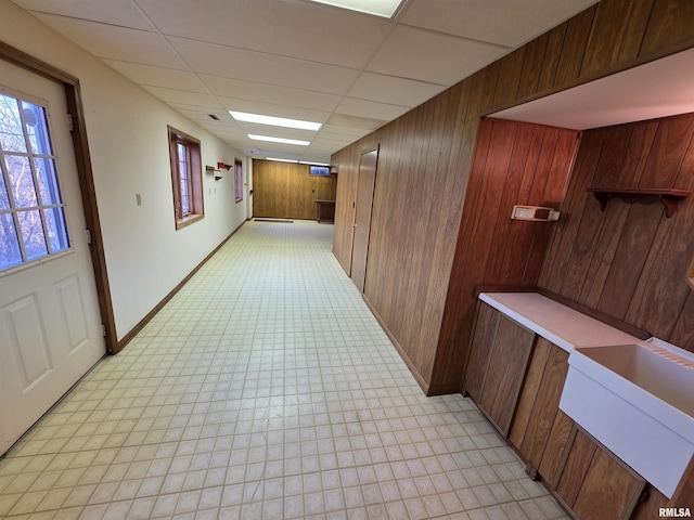 hallway featuring a paneled ceiling, light floors, plenty of natural light, and wooden walls