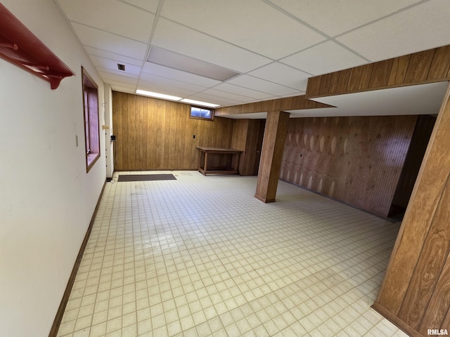 below grade area with a drop ceiling, wood walls, and light floors