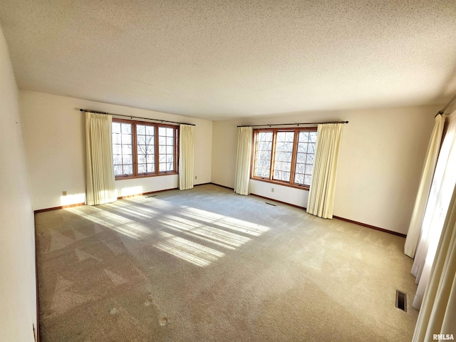 spare room featuring baseboards, visible vents, a textured ceiling, and light colored carpet