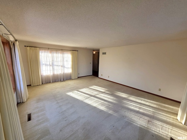 spare room featuring baseboards, visible vents, a textured ceiling, and light colored carpet