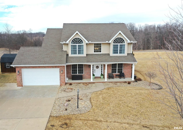 traditional-style house featuring a garage, concrete driveway, roof with shingles, covered porch, and brick siding