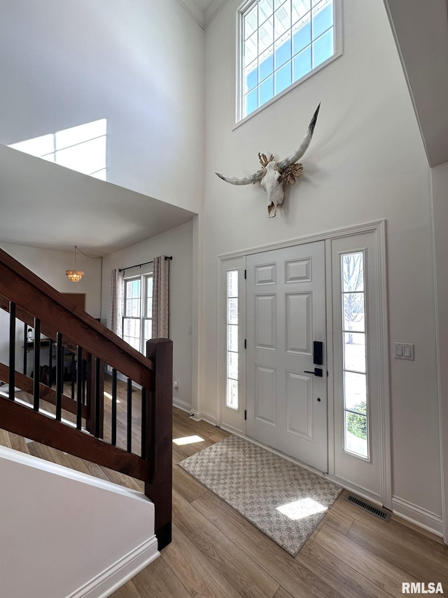 foyer entrance featuring wood finished floors, a towering ceiling, visible vents, stairs, and baseboards