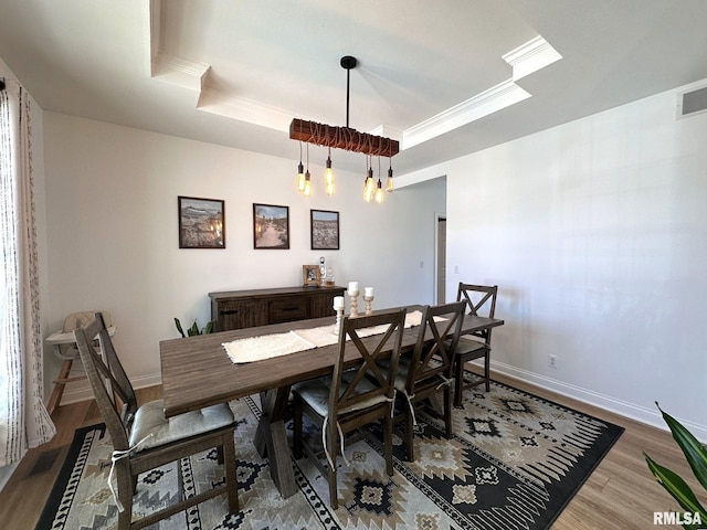 dining space featuring ornamental molding, a tray ceiling, baseboards, and wood finished floors