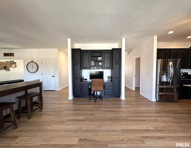 kitchen with visible vents, baseboards, light wood finished floors, stainless steel fridge, and built in desk