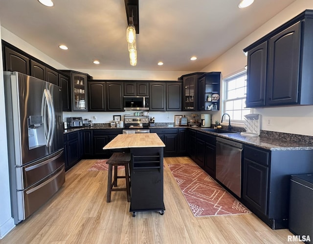 kitchen featuring light wood-style flooring, recessed lighting, a sink, appliances with stainless steel finishes, and glass insert cabinets