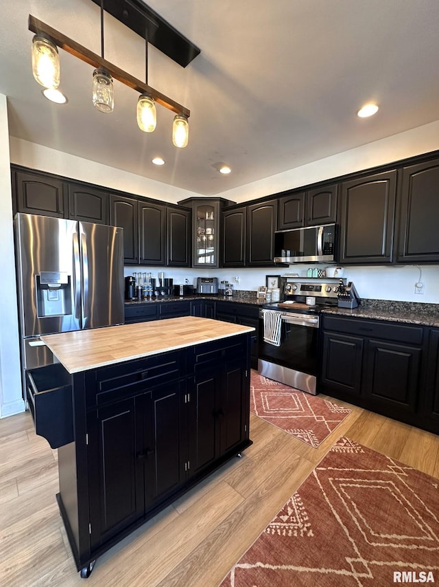 kitchen with appliances with stainless steel finishes, a center island, dark cabinetry, and light wood finished floors