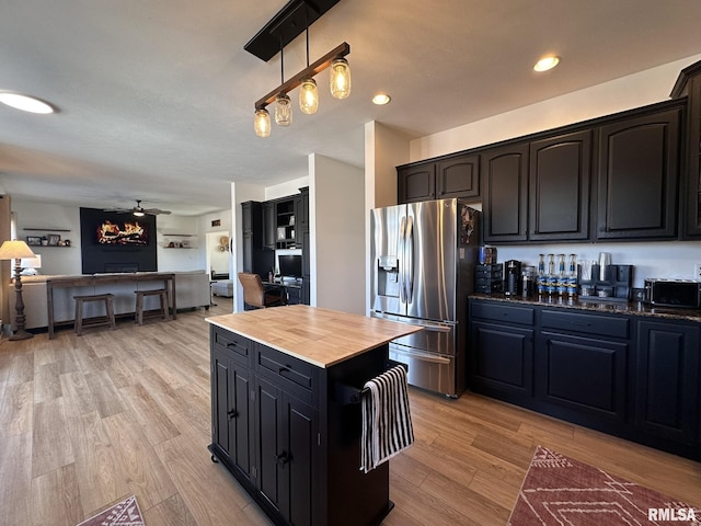 kitchen featuring light wood finished floors, dark cabinetry, a ceiling fan, open floor plan, and stainless steel fridge