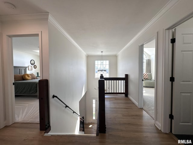 hall featuring baseboards, ornamental molding, wood finished floors, an inviting chandelier, and an upstairs landing