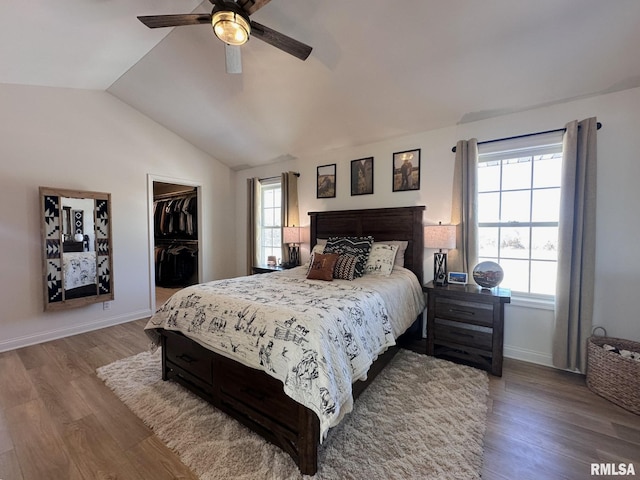 bedroom with vaulted ceiling, a spacious closet, wood finished floors, and baseboards