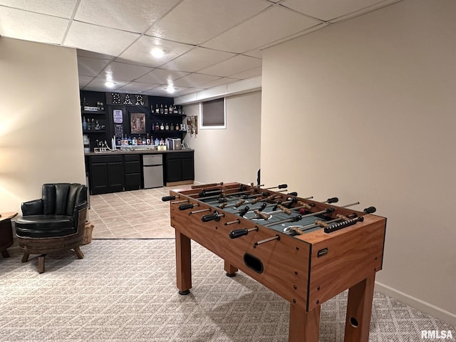 recreation room featuring light colored carpet, a paneled ceiling, baseboards, and a dry bar