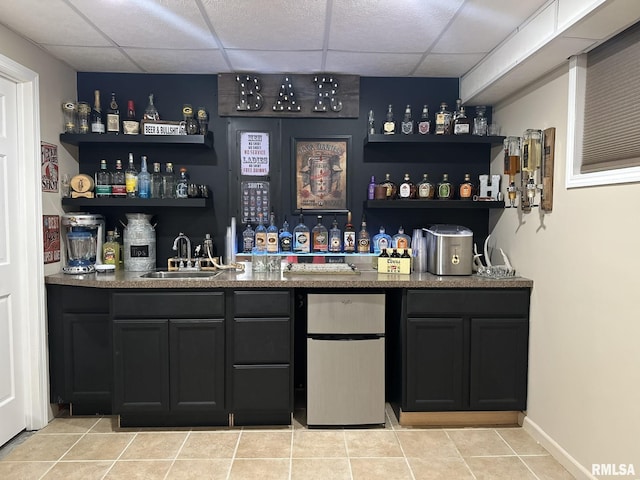 bar featuring light tile patterned floors, freestanding refrigerator, a sink, wet bar, and a drop ceiling