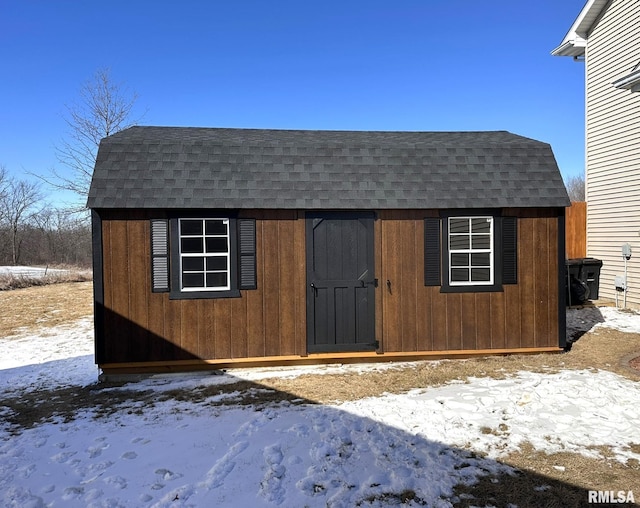 snow covered structure featuring a storage unit and an outbuilding