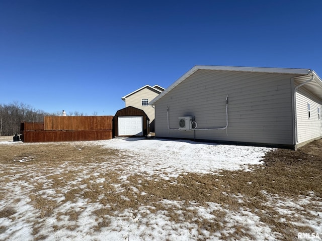 view of snow covered exterior featuring a garage, ac unit, fence, and an outbuilding